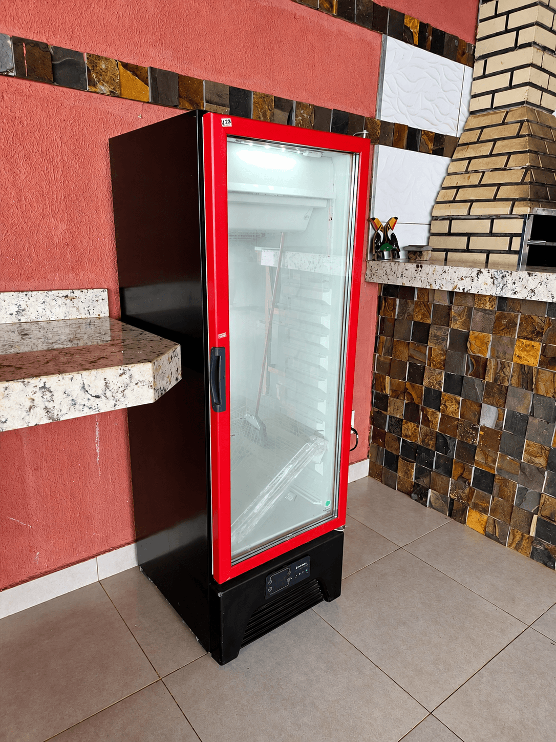 Cervejeira vermelha de porta de vidro na área coberta da Vila Agostinis, ao lado da churrasqueira.