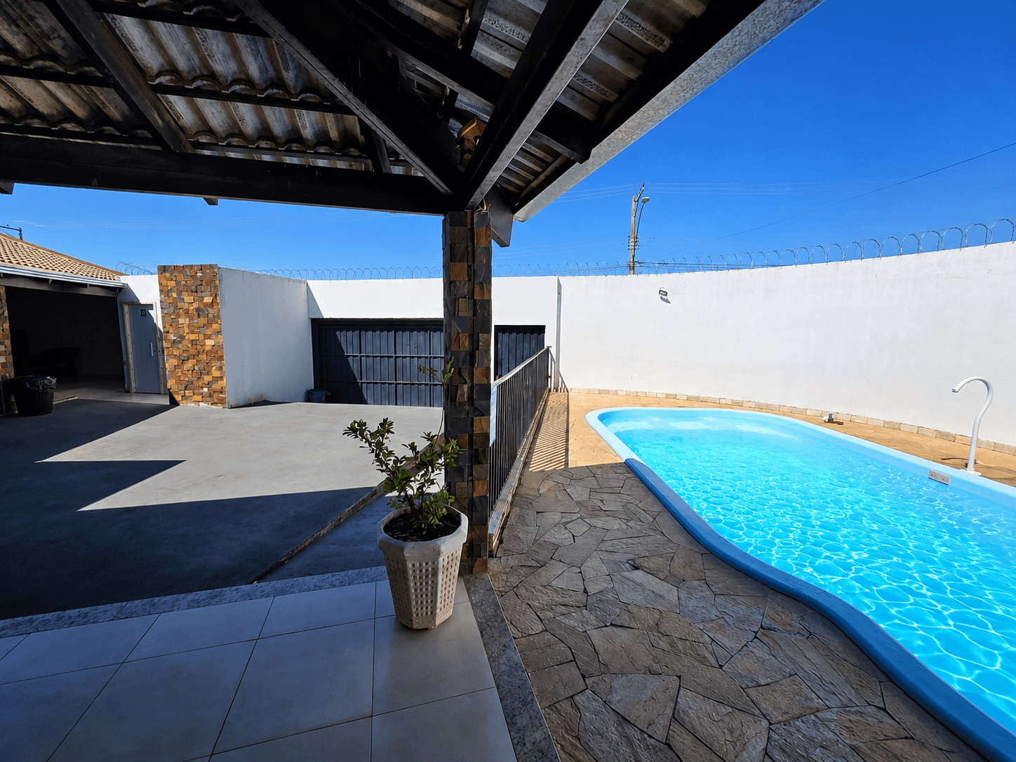 Vista lateral da piscina da Vila Agostinis a partir da área coberta, sob céu azul.