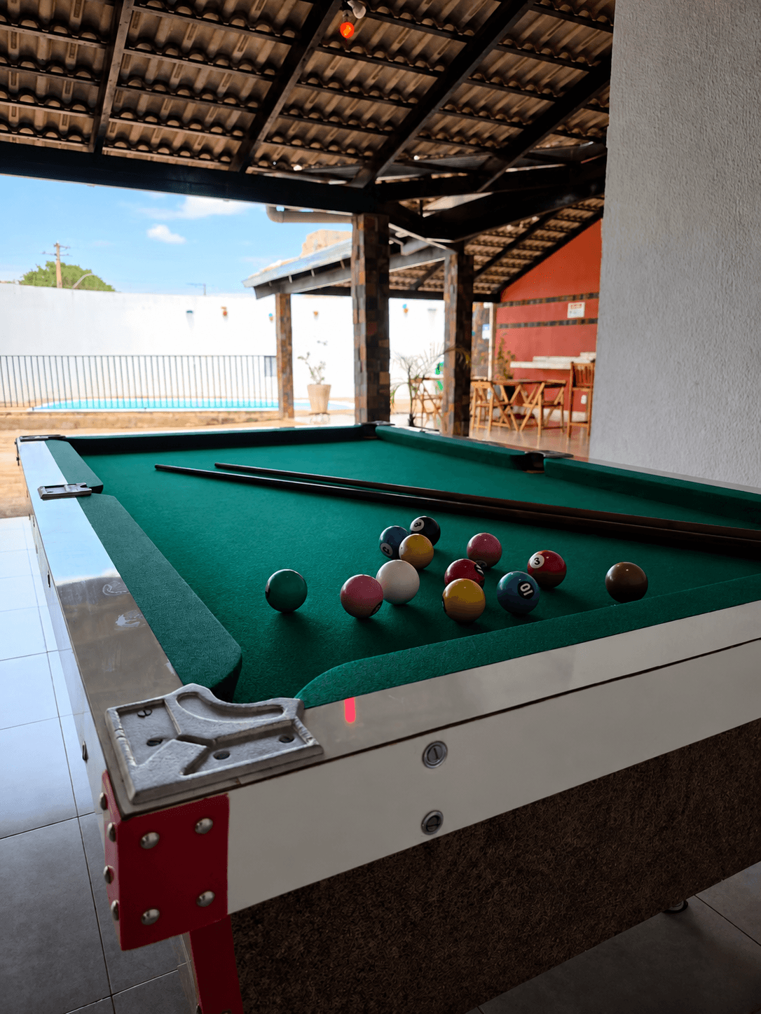 Bolas de sinuca sobre a mesa, com vista desfocada da área externa da Vila Agostinis ao fundo.